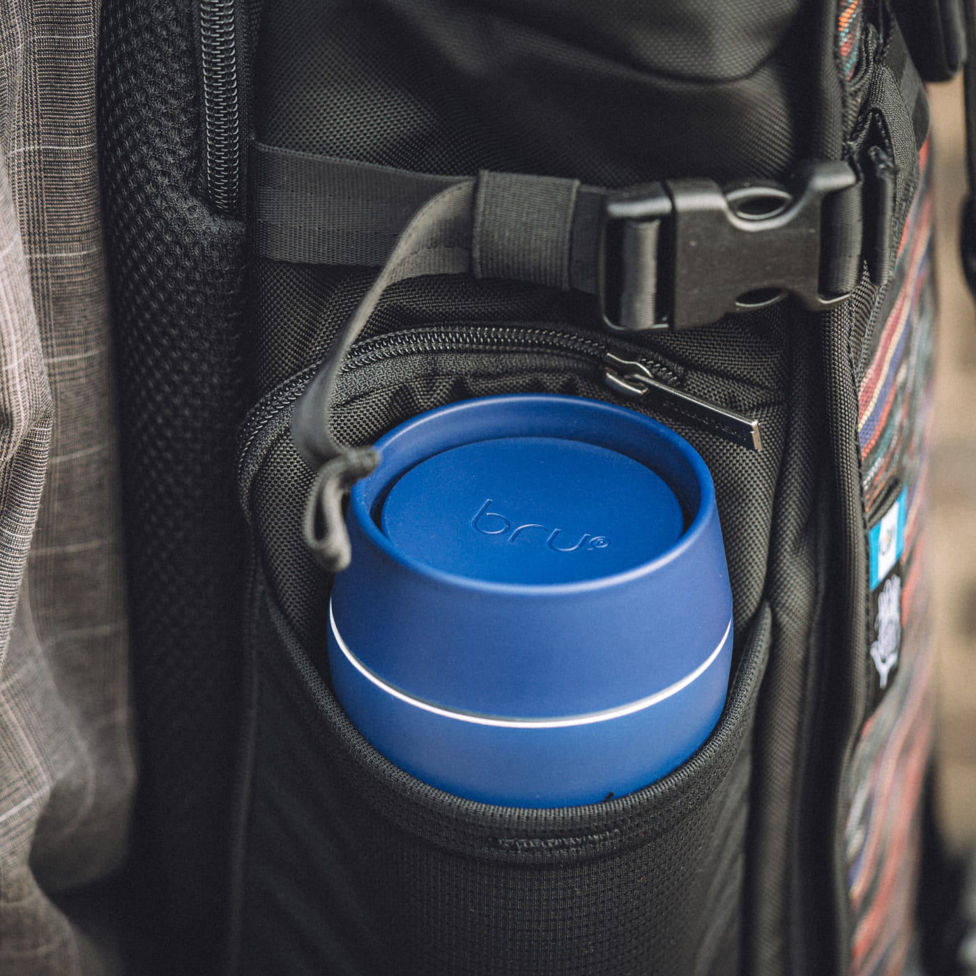100% Leakproof block: Blue bru ceramic travel mug sitting upright in the side pocket of a backpack, lid closed and leakproof for commuting