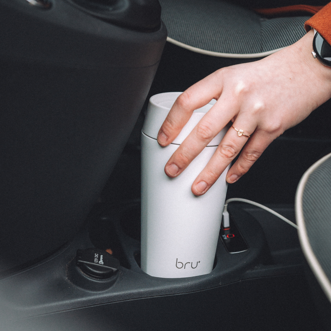 bru white insulated travel mug in a car cup holder with a person reaching for it
