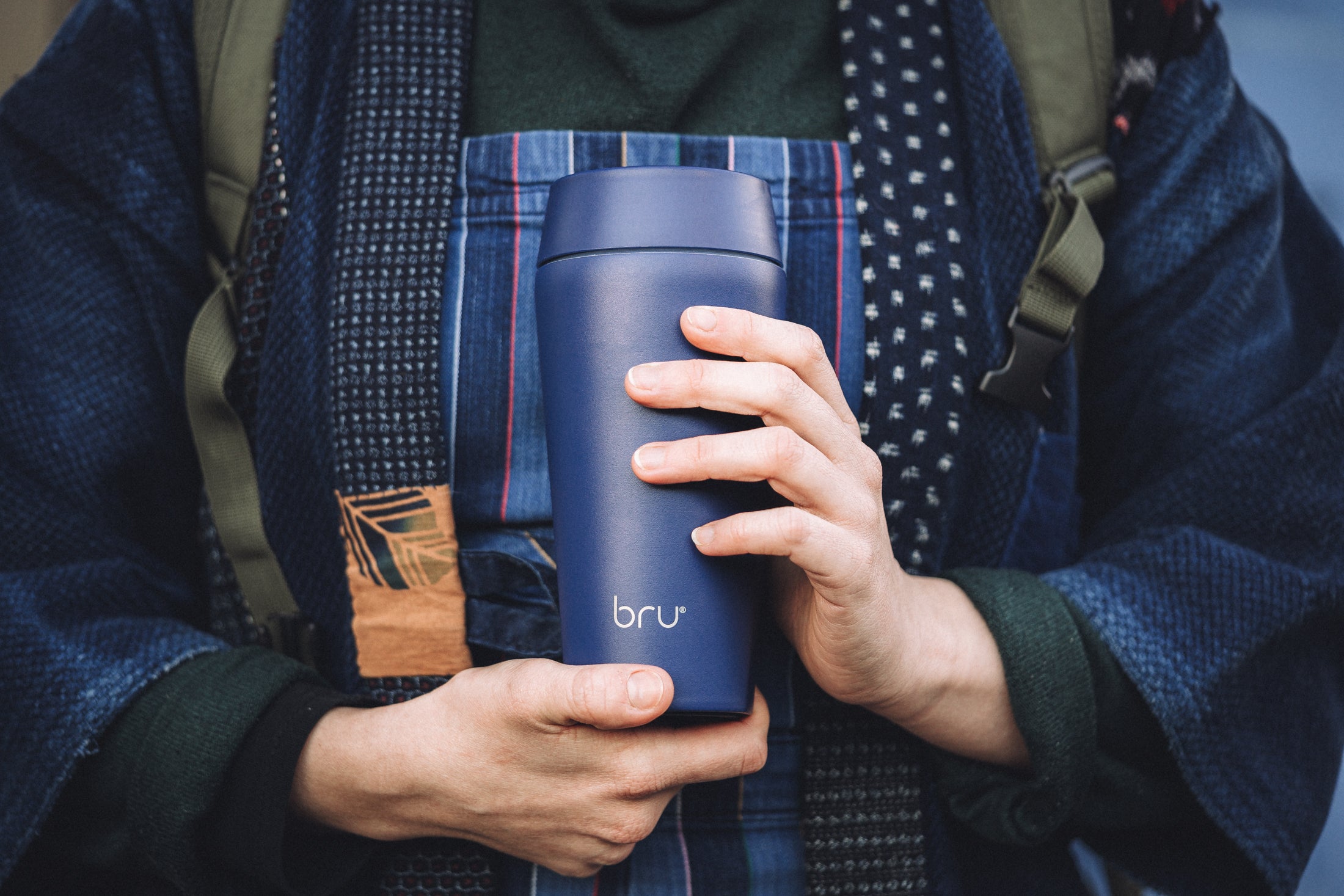 Bru-Cups ceramic-lined travel mug, blue 12oz, being held by a hipster wearing an apron