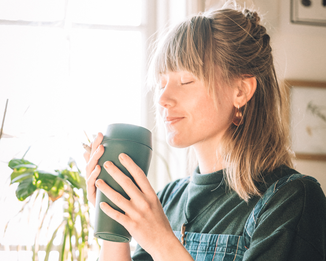 bru green insulated travel mug held by a person enjoying their coffee by a window